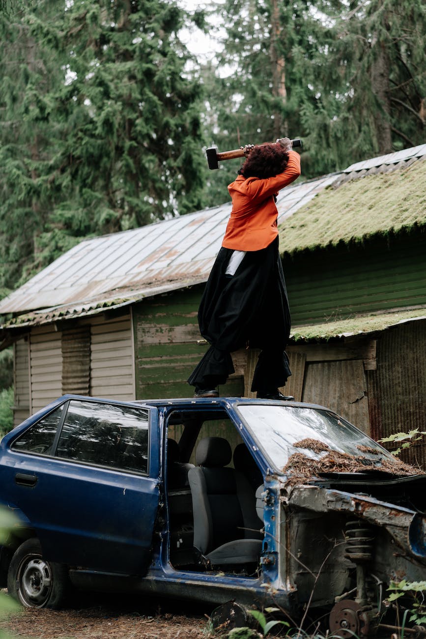person with a hammer standing on the roof of a car