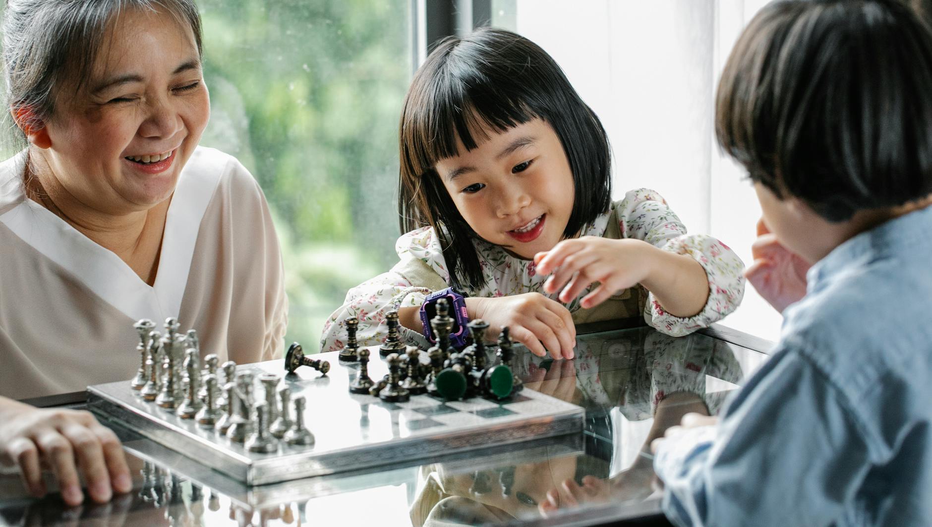 cute asian kids playing chess with help of positive grandmother