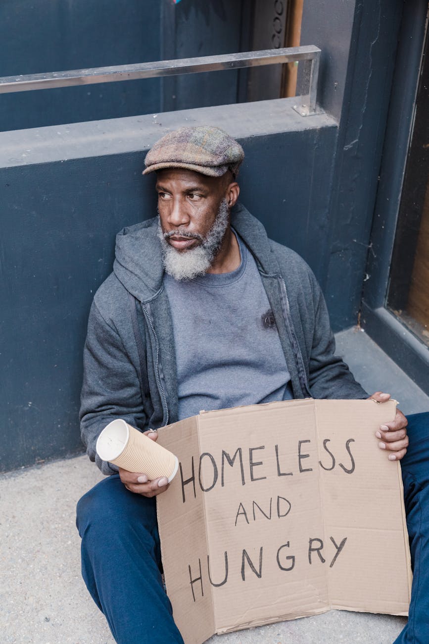 man sitting on a pavement holding a sign of homeless and hungry
