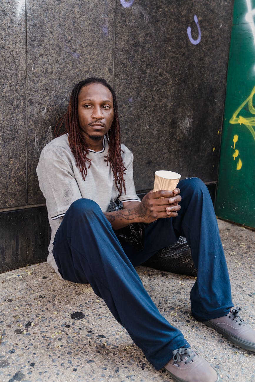 man sitting and leaning on a wall holding a paper cup