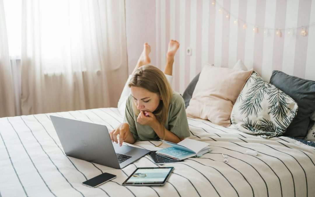 woman lying on bed while using a laptop