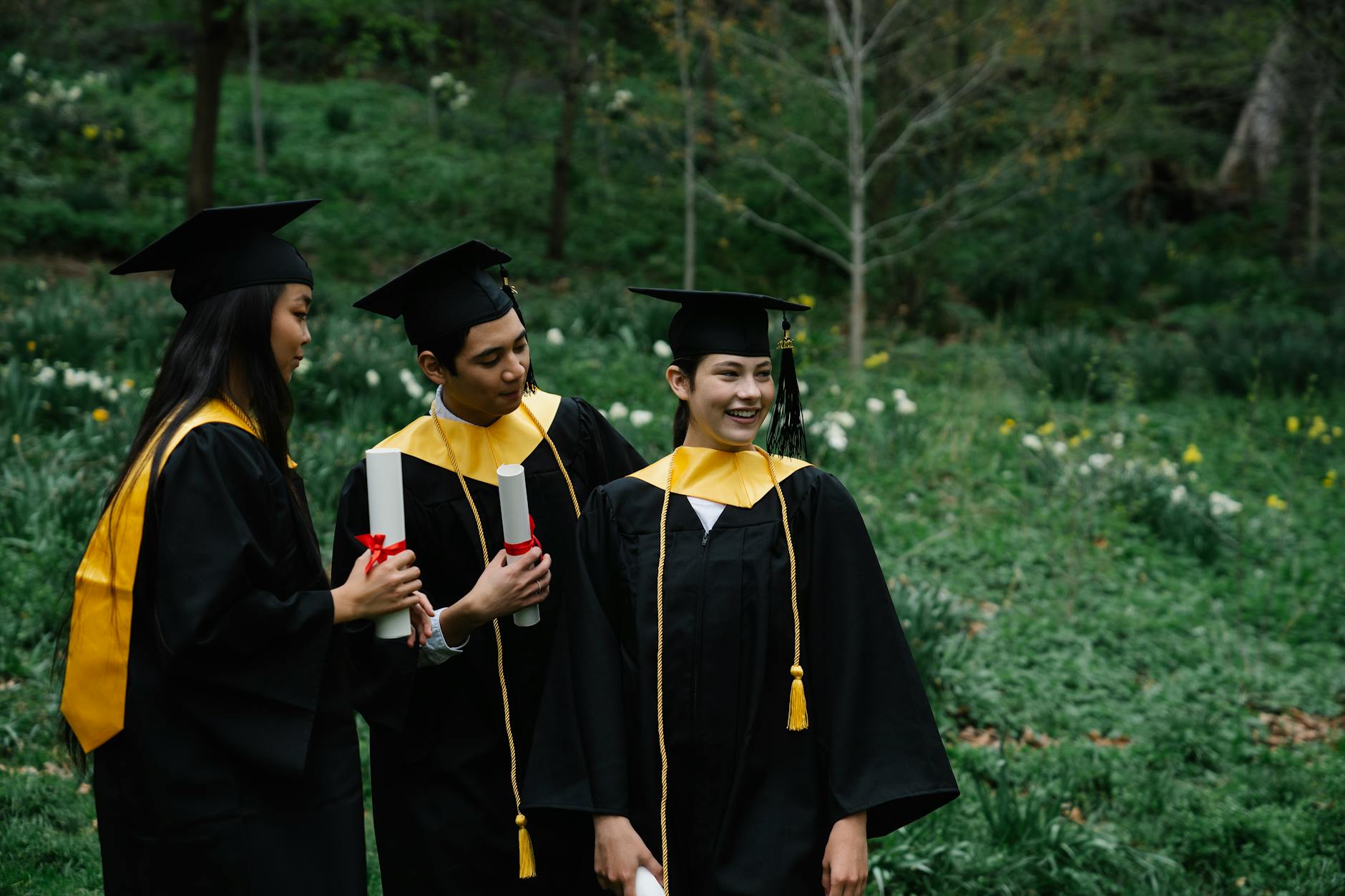 happy students in graduation mantles in park