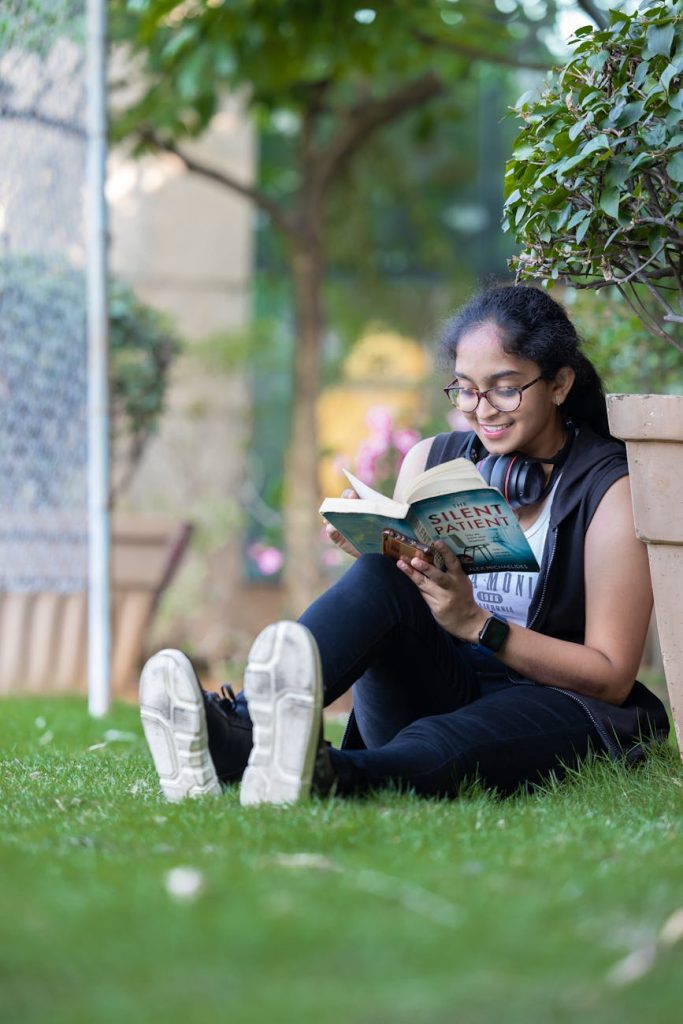 Current image: a girl sitting on the grass in a park and reading a book