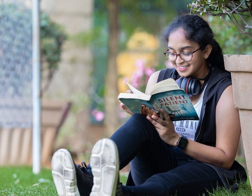 a girl sitting on the grass in a park and reading a book