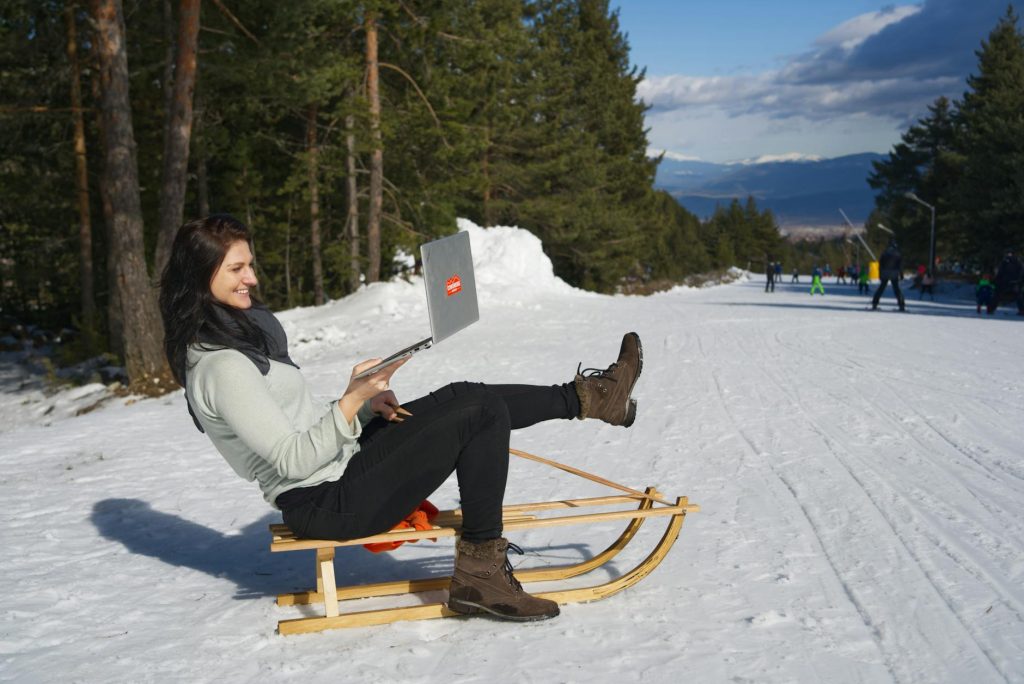 Current image: woman sitting on wooden sled using silver macbook