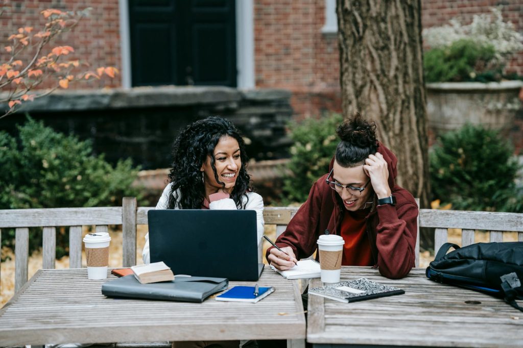 Current image: diverse students working together at table with laptop in park
