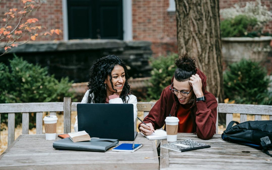 diverse students working together at table with laptop in park
